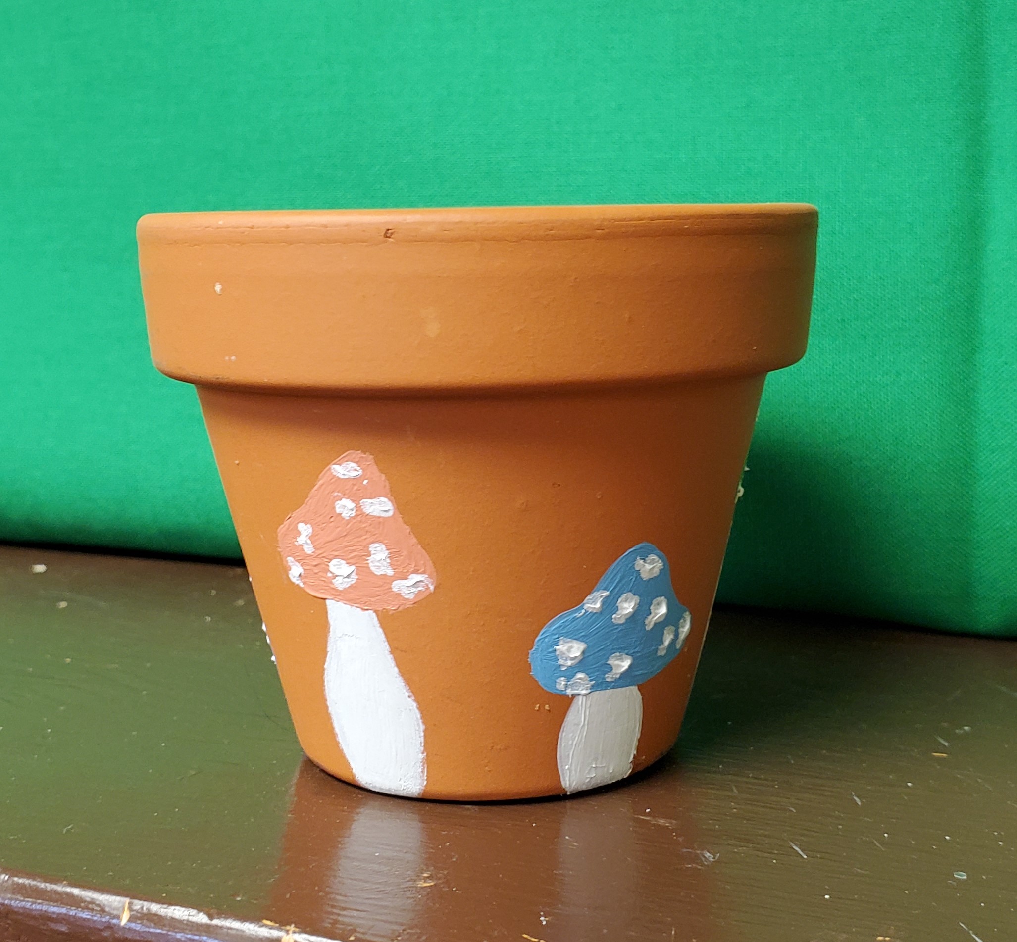 A brown planter with mushrooms painted on it in front of a green wall.
