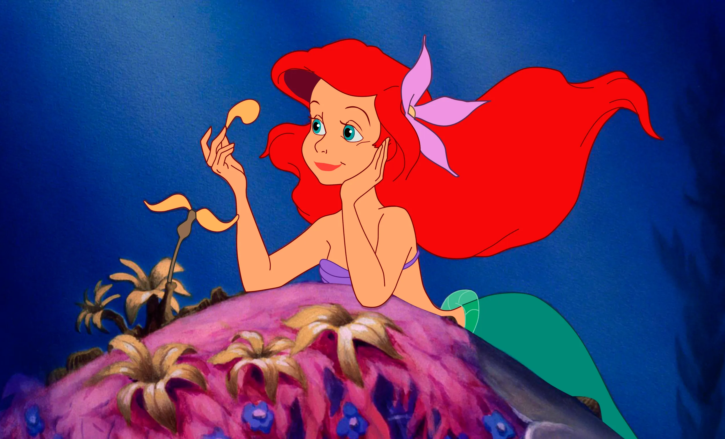 Ariel in "The LIttle Mermaid" looking at a plant petal while learning on a rock.