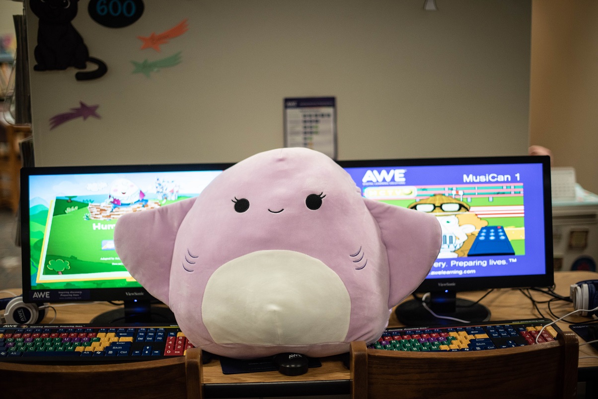 A stingray Squishmallow ontop of children computers.