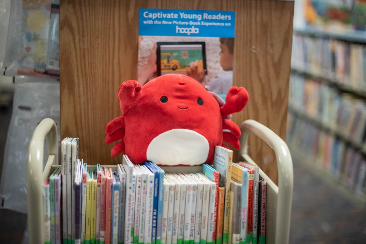 A small red crab Squishmallow on top of a cart of books.