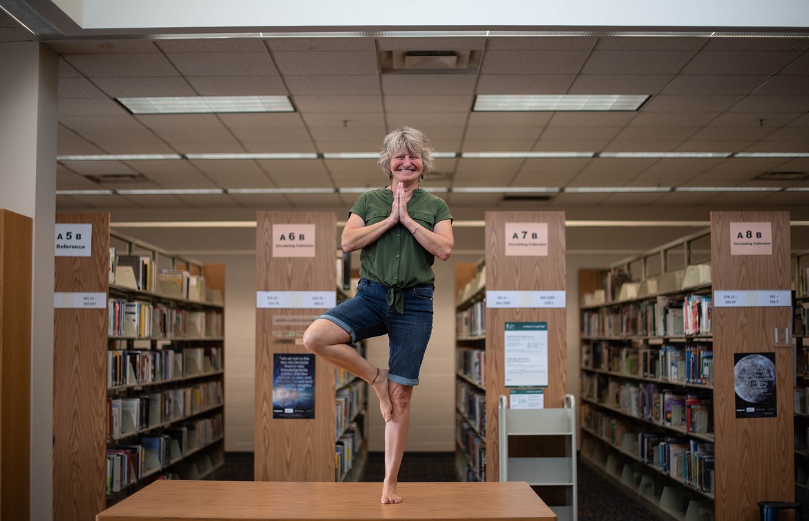 Bonnie Dwier is standing on a table in a standing yoga position with hands clasped together