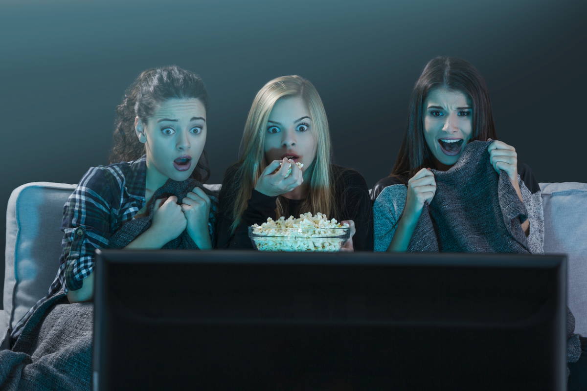 Three girls watching a scary movie eating popcorn.