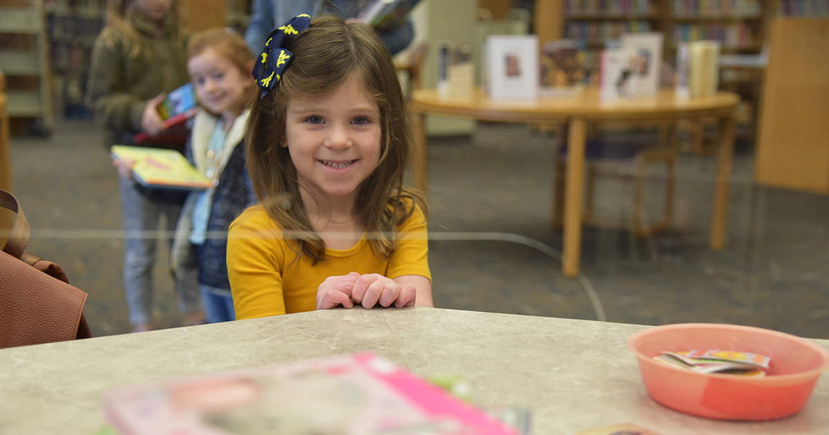 A child smiling checking out books at the library.